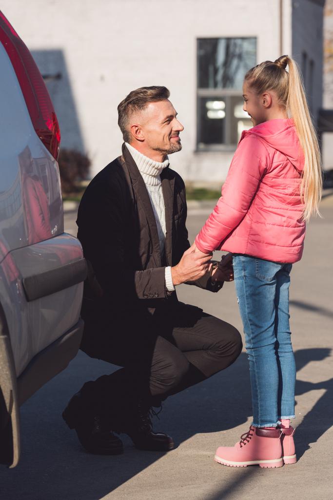 Papa hand in hand voor dochter in de buurt van auto  - Foto, afbeelding