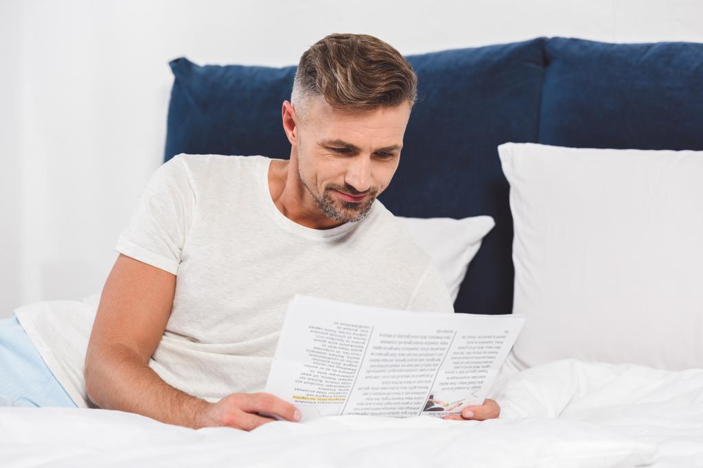 ハンサムな男のベッドで新聞を読む - 写真・画像