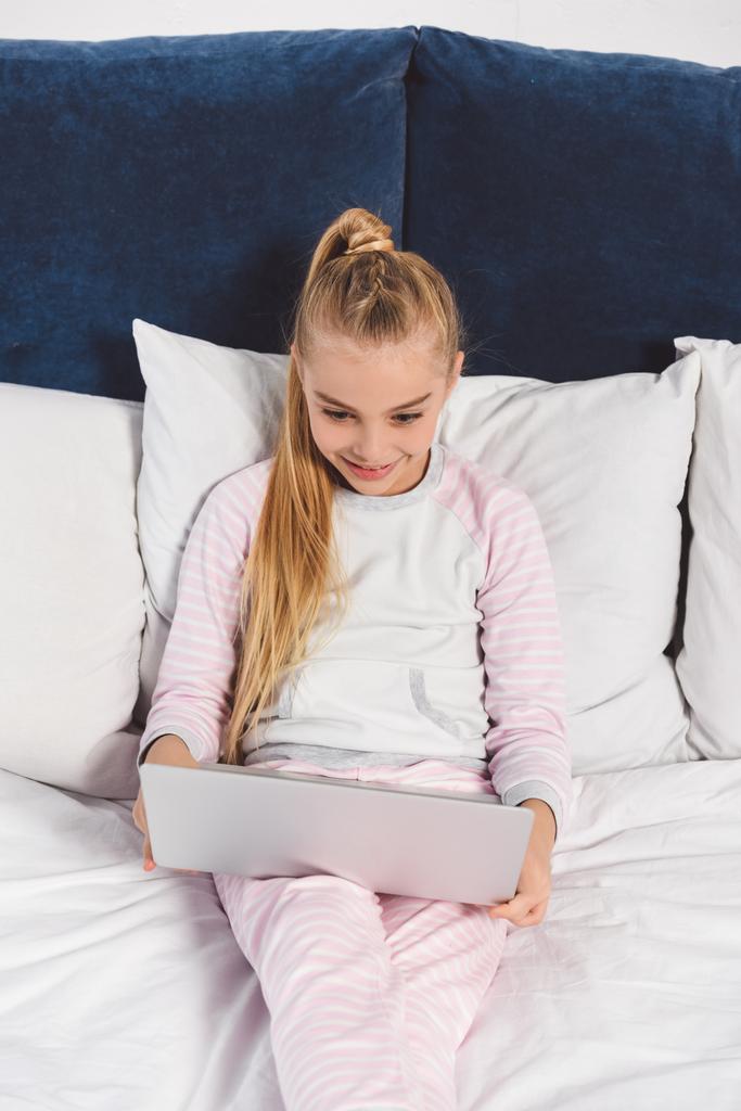 Criança pré-adolescente feliz deitada na cama com laptop
  - Foto, Imagem