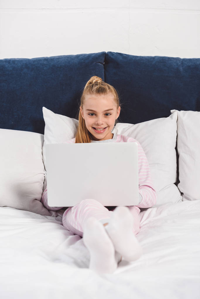 Vrolijke preteen kind met laptop in slaapkamer  - Foto, afbeelding