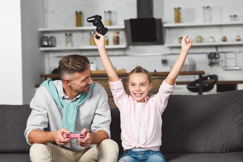 onnellinen tytär riemuitsee voitosta pelatessaan videopeliä isän kanssa
 - Valokuva, kuva