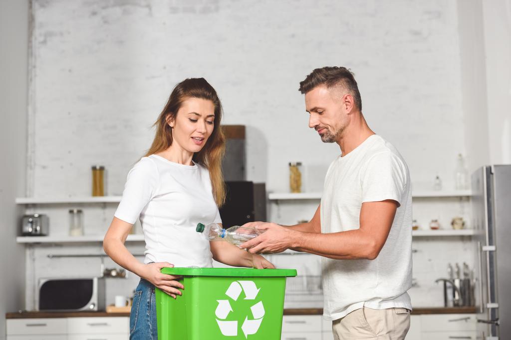 pareja de adultos poniendo botellas de plástico vacías en la caja verde de reciclaje en la cocina
 - Foto, imagen