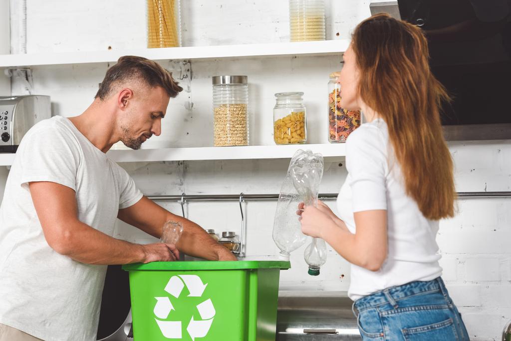 доросла пара поклала порожні пластикові пляшки в зелену коробку зі знаком переробки
 - Фото, зображення
