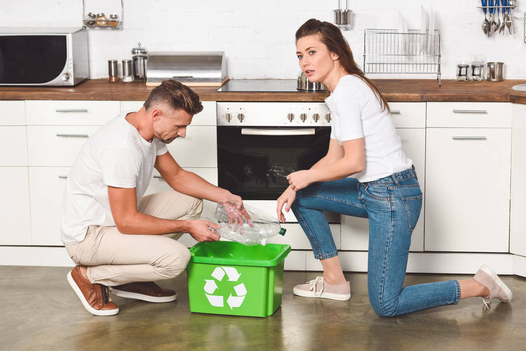 Coppia di adulti mettere bottiglie di plastica vuote nel riciclaggio scatola verde in cucina
 - Foto, immagini