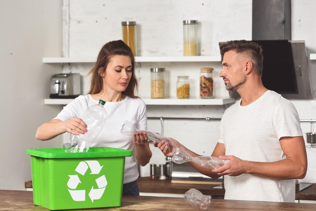Mann und Frau stehen in Küche und legen leere Plastikflaschen in Recyclingbox  - Foto, Bild