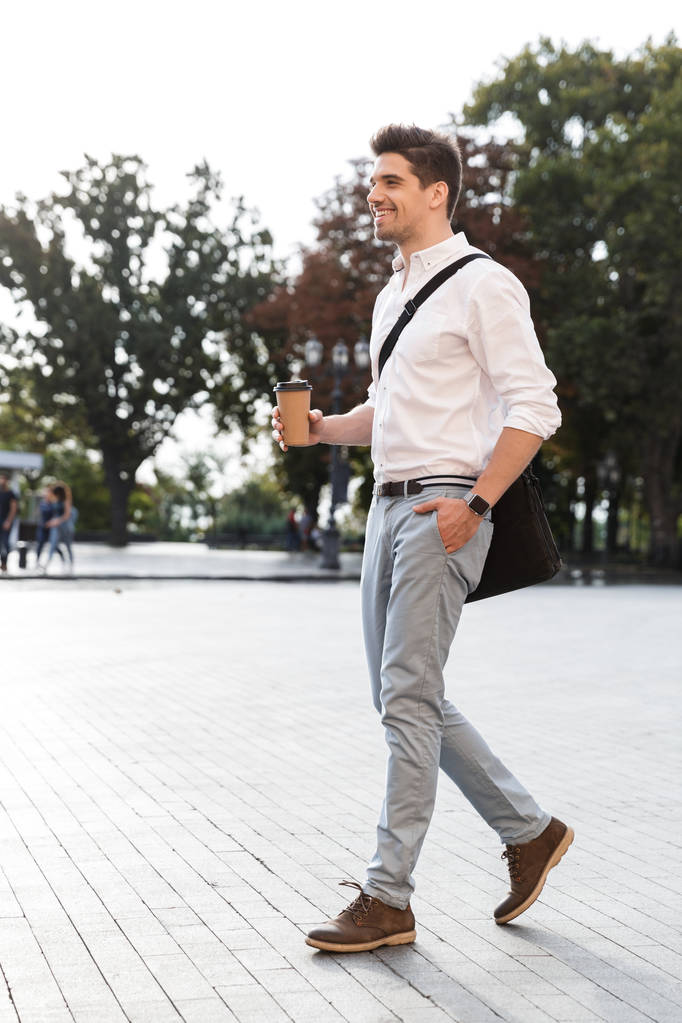 Fiducioso uomo d'affari vestito di camicia che cammina all'aperto per la strada della città, tenendo caffè da asporto
 - Foto, immagini