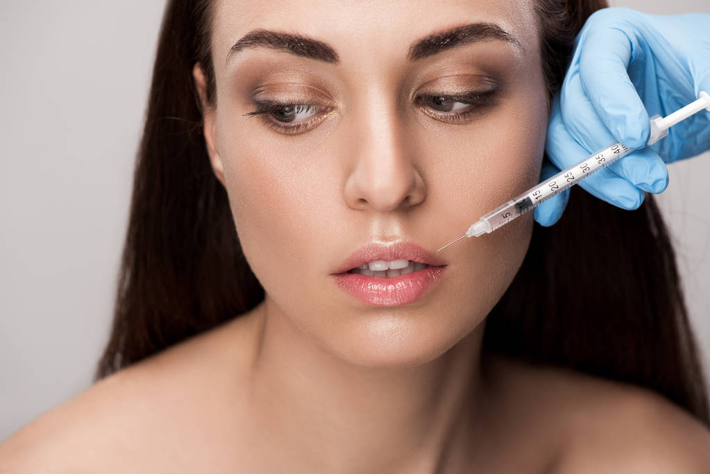 doctor making beauty injection into lips for attractive girl isolated on grey - Photo, Image