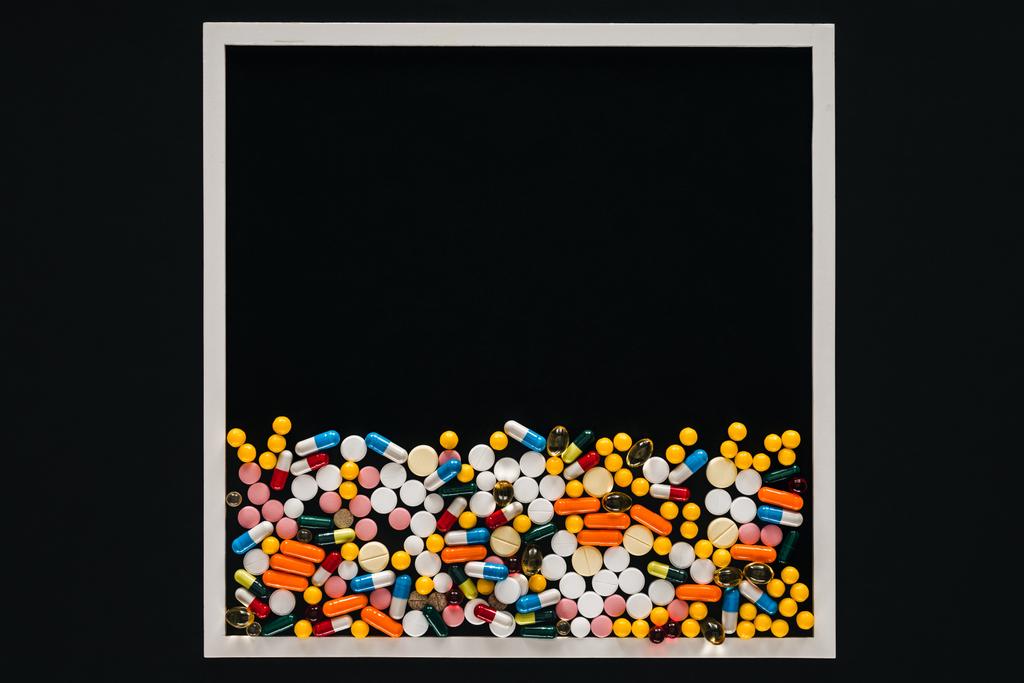 Blick von oben auf Rahmen mit Stapel bunter Pillen isoliert auf schwarz - Foto, Bild