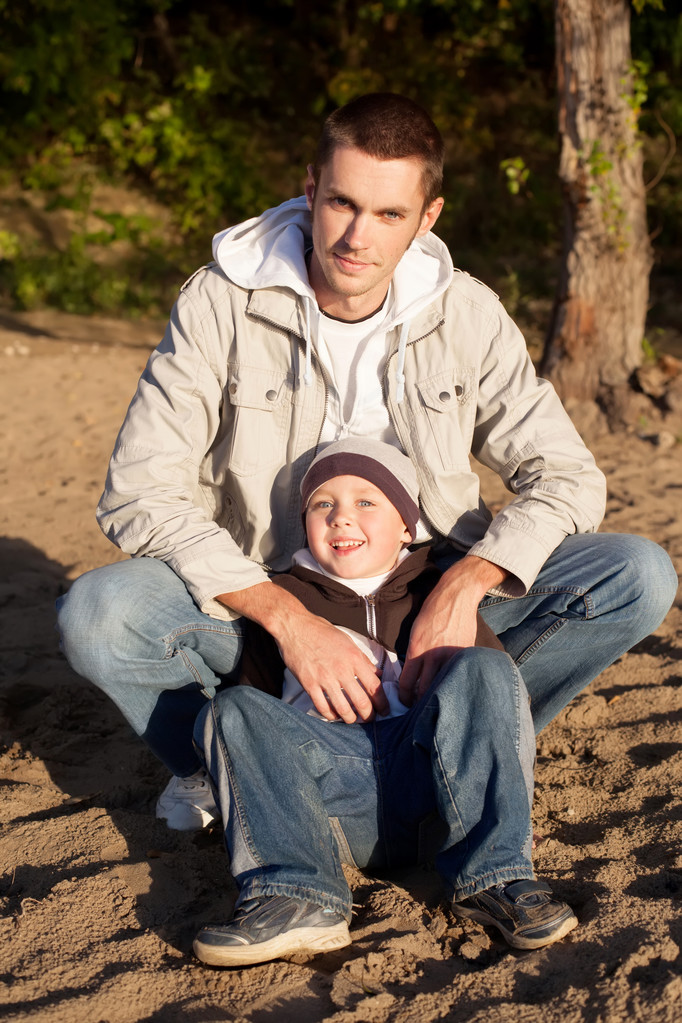 Молодой отец и его маленький сын сидят и смотрят в камеру
 - Фото, изображение