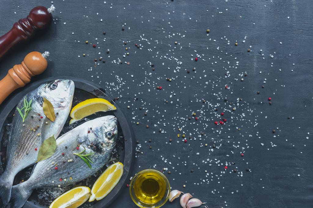 içinde tepsi malzemelerle çiğ balık üstten görünüm siyah masada tuz ve biber - Fotoğraf, Görsel