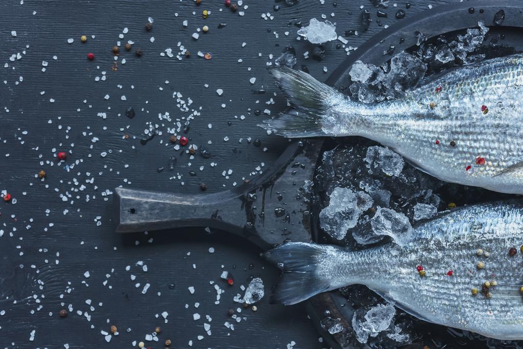 вид сырой рыбы в лотке на черном столе, покрытом солью и перцем
 - Фото, изображение