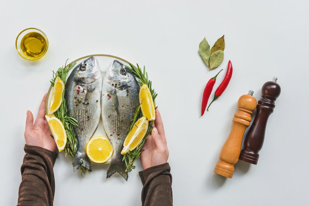 ローズマリーとレモンで装飾された魚と板を取って女性の部分的なビュー  - 写真・画像