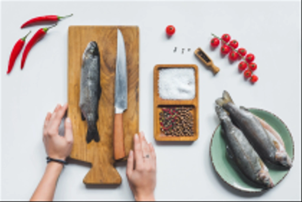 partial view of female hands on wooden board with knife and raw fish near ingredients on white table - Photo, Image
