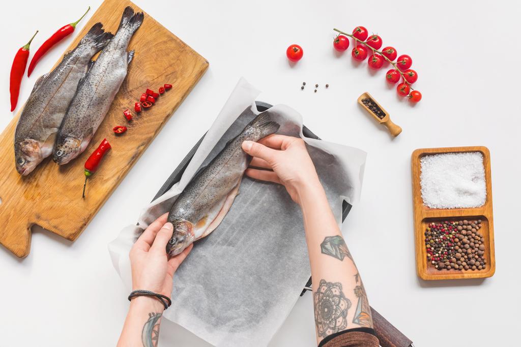 partial view of woman putting uncooked fish in tray with baking paper on white table with ingredients - Photo, Image