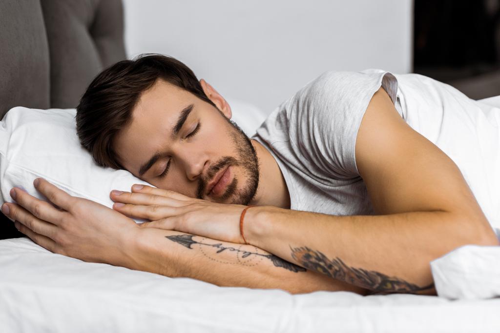 όμορφος γενειοφόρος τατουάζ νεαρός άνδρας κοιμάται στο κρεβάτι  - Φωτογραφία, εικόνα