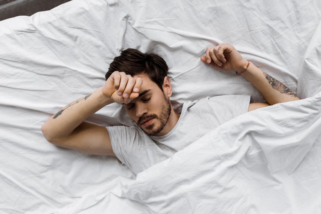 Draufsicht auf schlafenden jungen Mann, der zu Hause unter Decke im Bett liegt - Foto, Bild