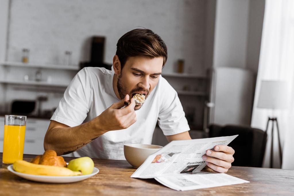 νεαρός άνδρας έχοντας δημητριακά για το πρωινό και διαβάζοντας εφημερίδα στο σπίτι - Φωτογραφία, εικόνα