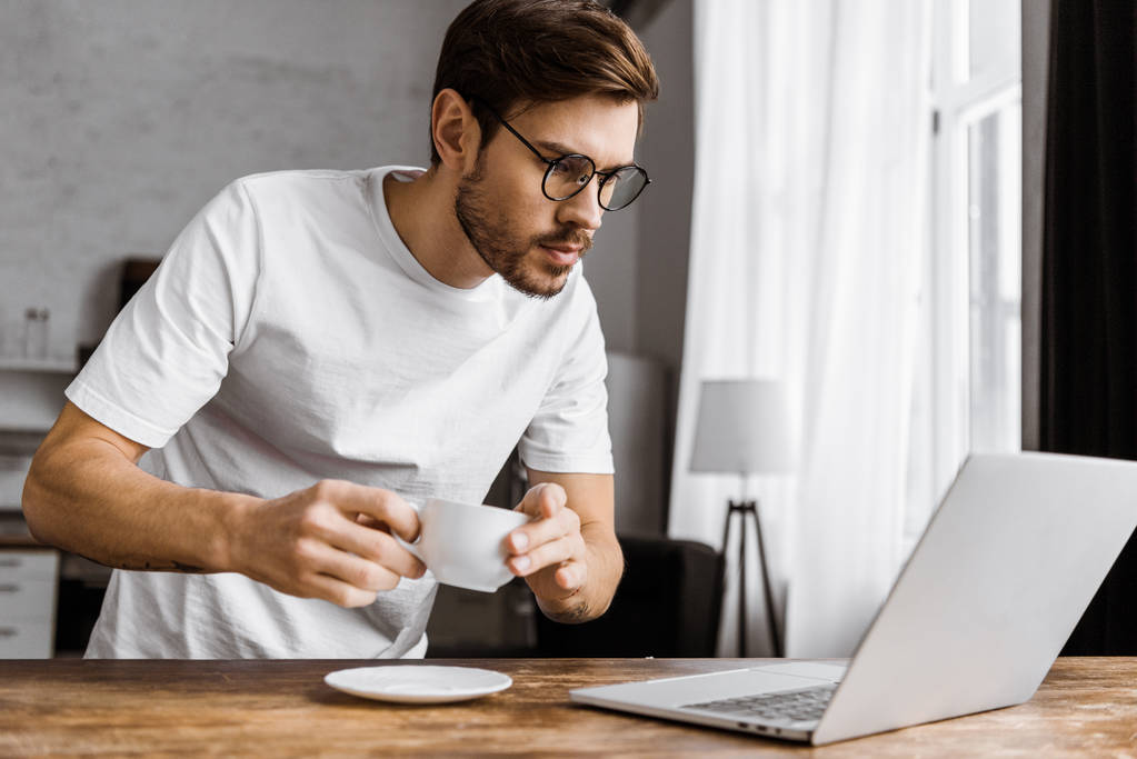 привлекательный молодой фрилансер с кофе, работающий с ноутбуком дома
 - Фото, изображение