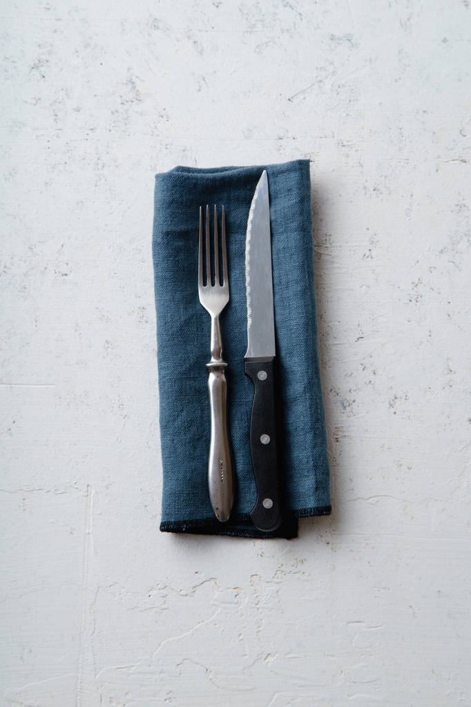 Cuchillo y tenedor sobre servilleta textil azul sobre fondo de piedra de hormigón
 - Foto, Imagen