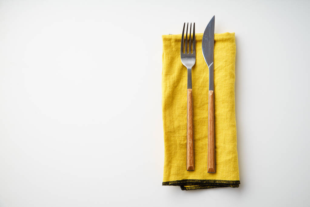Μαχαίρι και πιρούνι σε χαρτοπετσέτα κίτρινο ύφασμα που απομονώνονται σε λευκό φόντο, γκρο πλαν  - Φωτογραφία, εικόνα