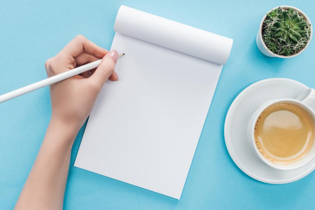oříznutý pohled člověk píšící v prázdné notebook s šálkem kávy na modrém pozadí - Fotografie, Obrázek