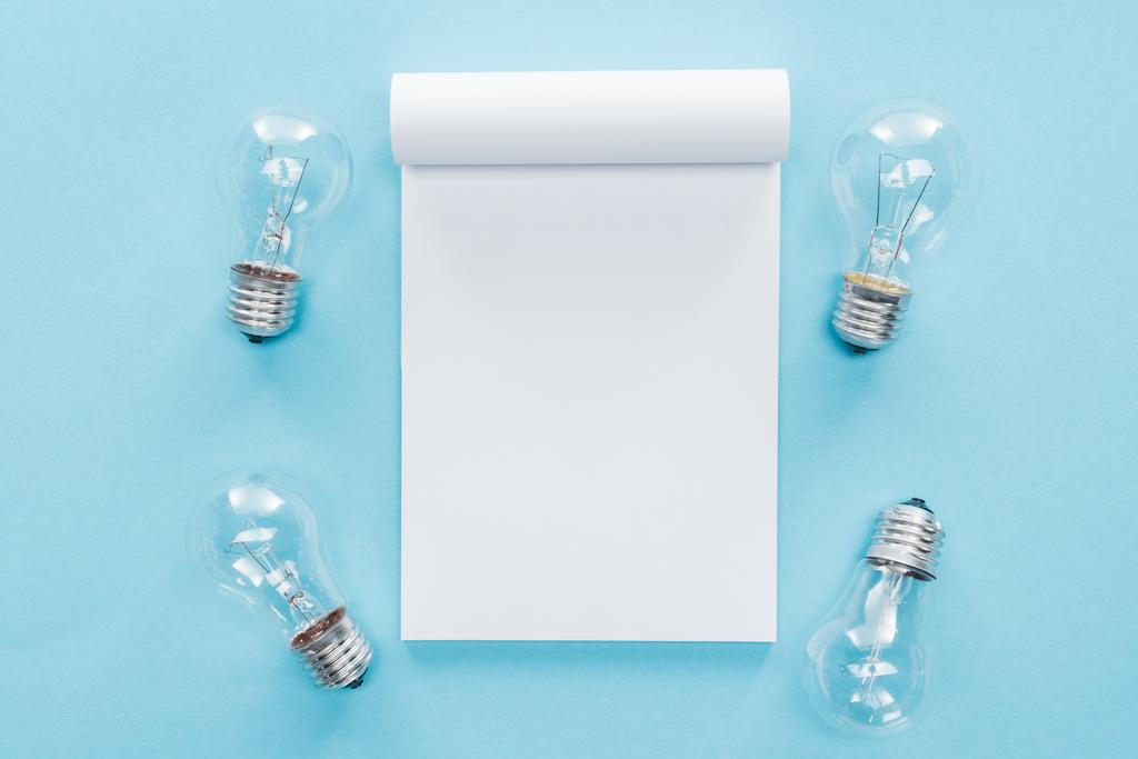vista superior del cuaderno en blanco con bombillas sobre fondo azul, lluvia de ideas y concepto de idea
 - Foto, Imagen