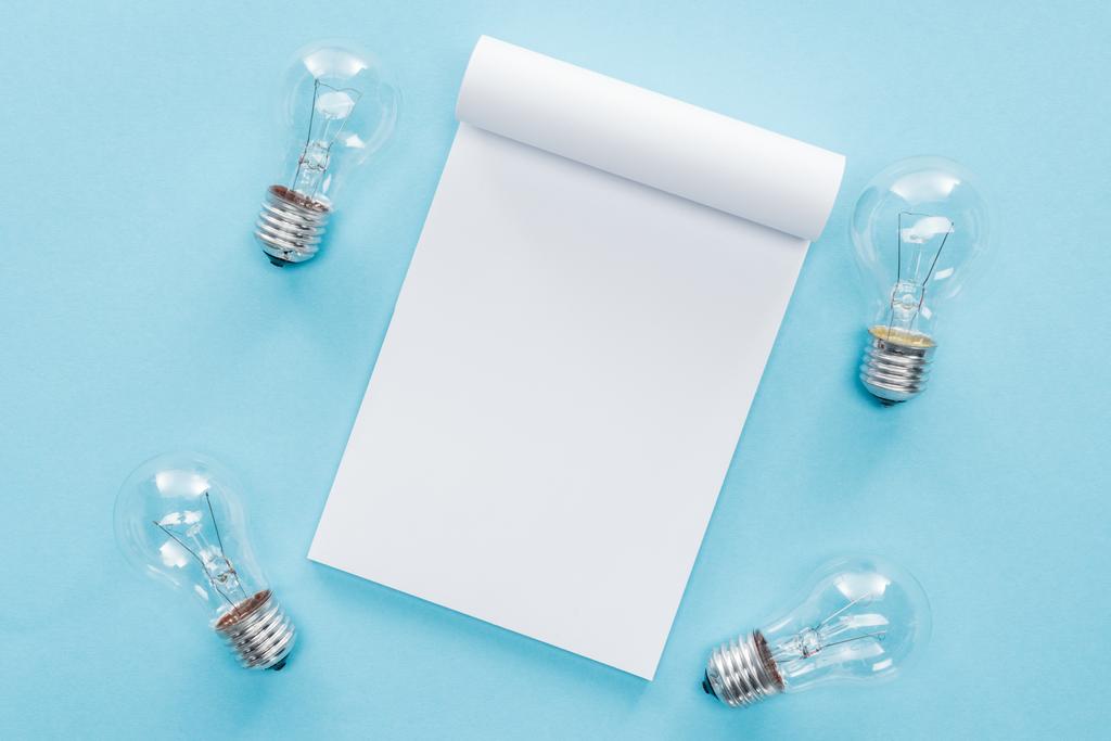 top view of blank notebook with light bulbs on blue background, having idea concept - Photo, Image