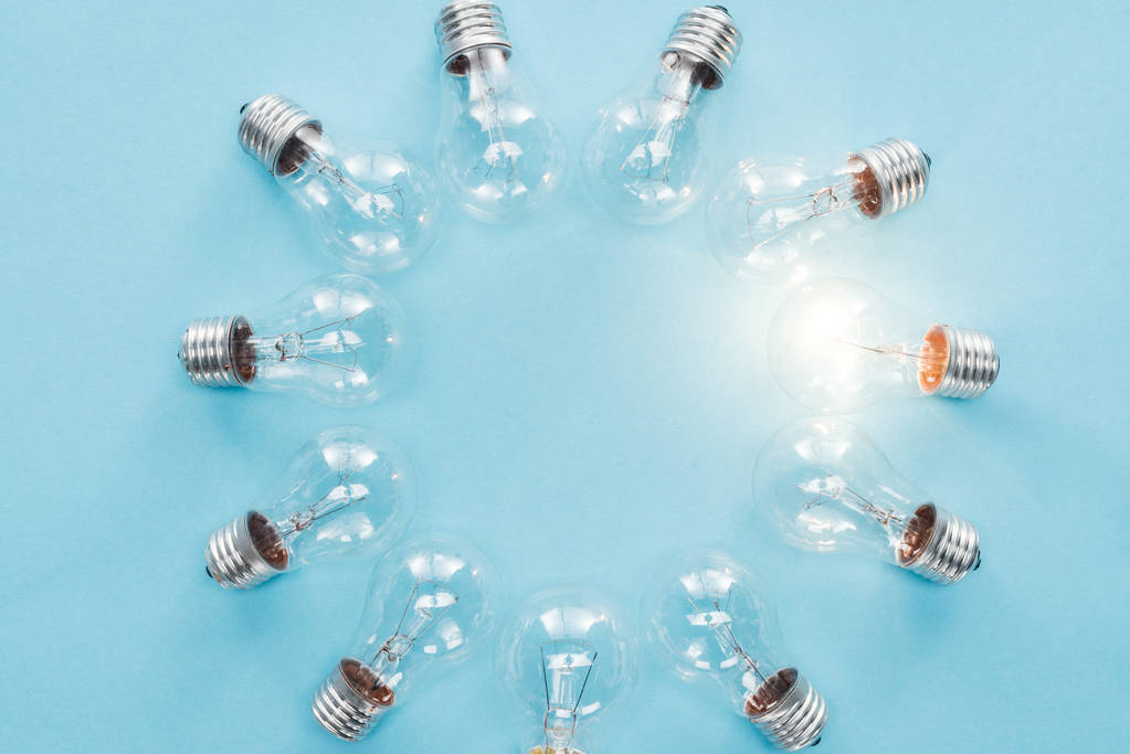 top view of light bulbs in circle and one of them glowing on blue background, having new idea concept - Photo, Image