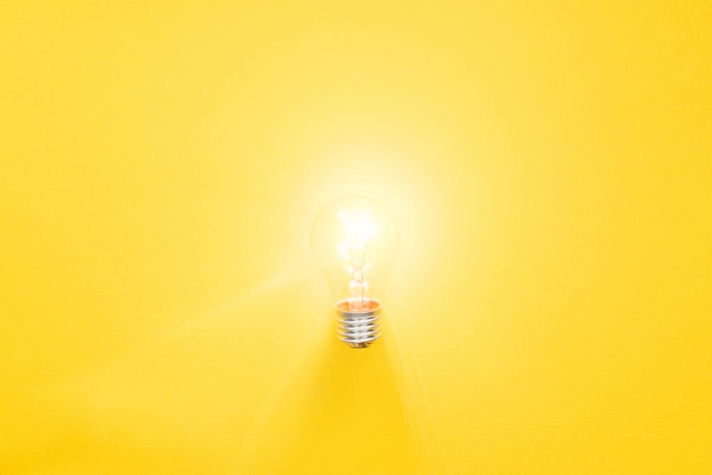 黄色の背景に電球を点灯し、新しいアイデアの概念を持っている - 写真・画像