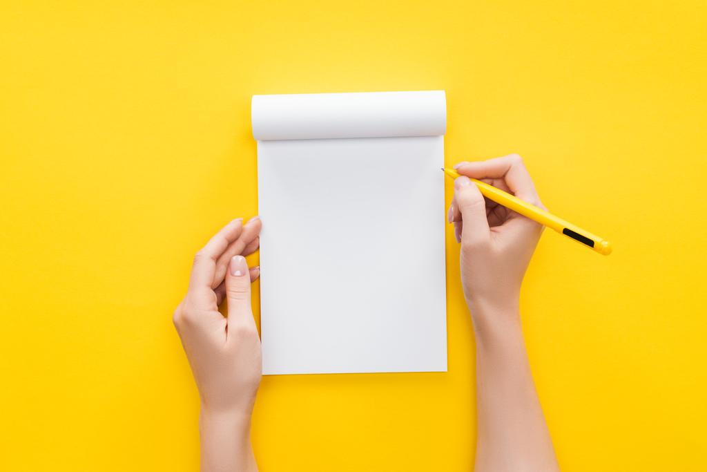  vista parziale persona che tiene penna su notebook vuoto su sfondo giallo
 - Foto, immagini