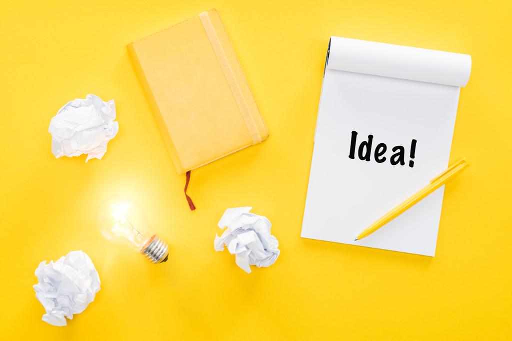 notebook com palavra 'ideia', bolas de papel desmoronadas e lâmpada brilhante, tendo novo conceito de ideias
 - Foto, Imagem