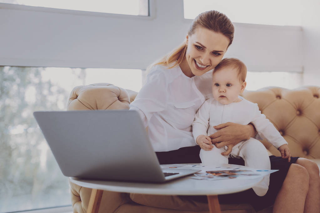 Amable joven madre viendo dibujos animados en el ordenador portátil con su bebé
 - Foto, imagen