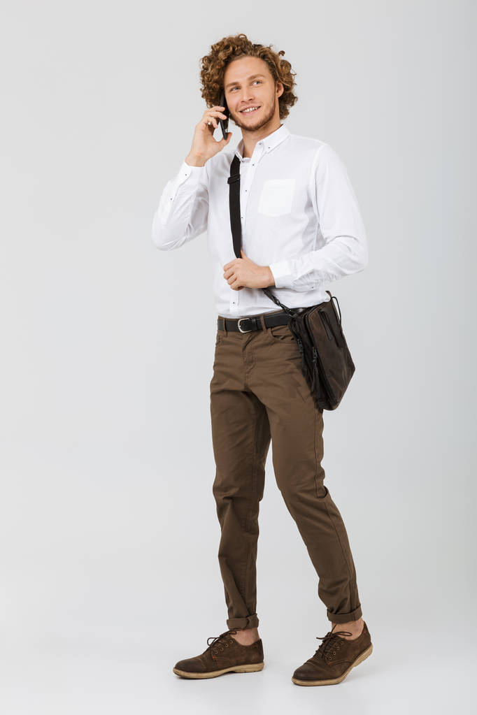 Полнометражный портрет улыбающегося бизнесмена, одетого в рубашку изолированного на белом фоне, разговаривающего по мобильному телефону
 - Фото, изображение