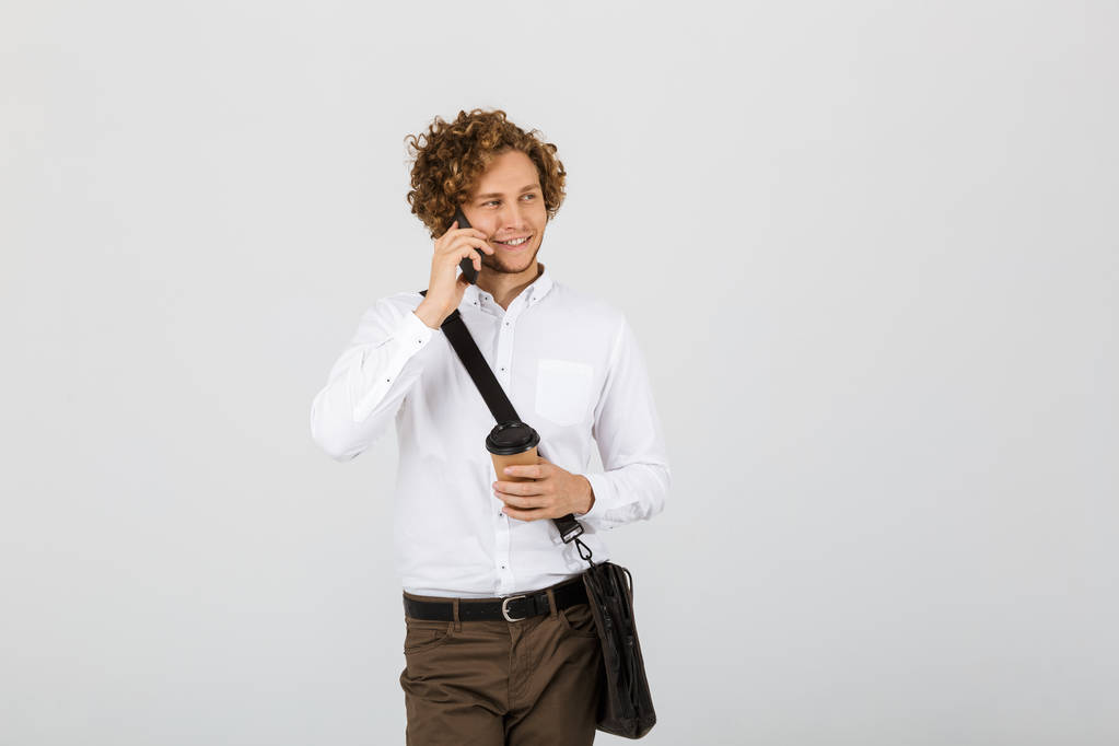 Portrait d'un homme d'affaires souriant vêtu d'une chemise isolée sur fond blanc, parlant sur un téléphone portable, tenant une tasse de café
 - Photo, image