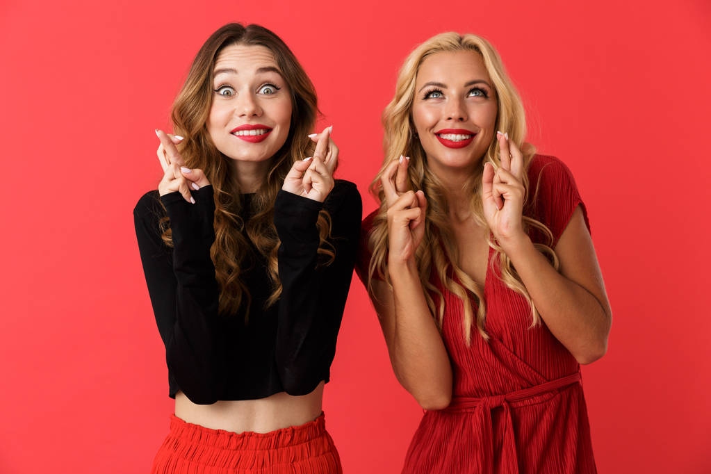 Image de jeunes amies excitées femmes isolées sur fond rouge montrant un geste plein d'espoir
. - Photo, image
