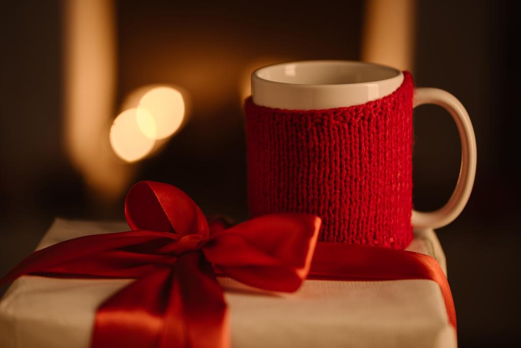 knitted mug and present with bow on blurred background - Photo, Image