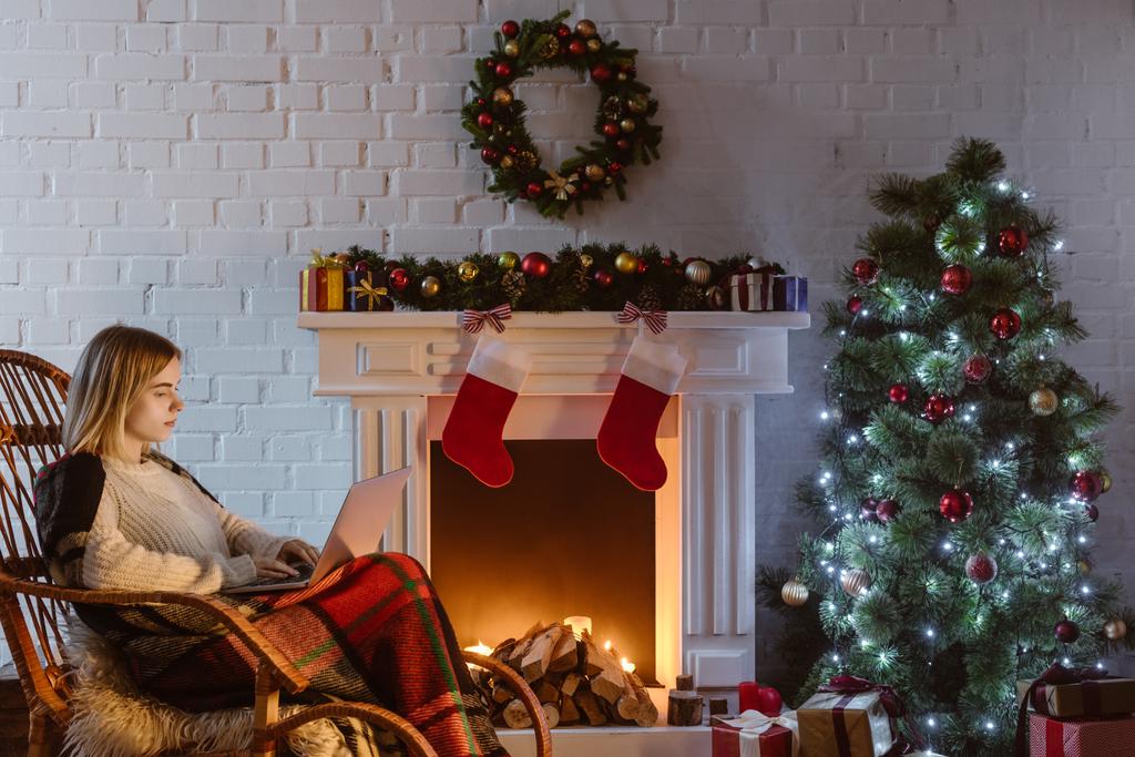  jovem mulher em vime cadeira de balanço usando laptop na sala de estar decorada para o Natal
  - Foto, Imagem