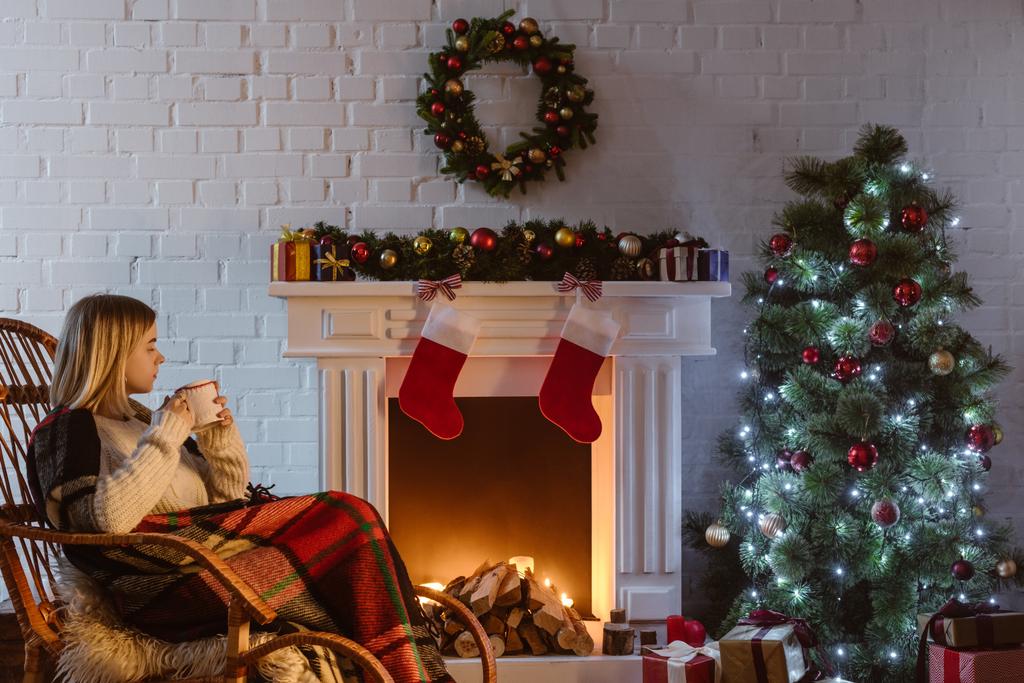  giovane donna su sedia a dondolo in vimini con in mano una tazza di caffè in soggiorno decorato per Natale
  - Foto, immagini