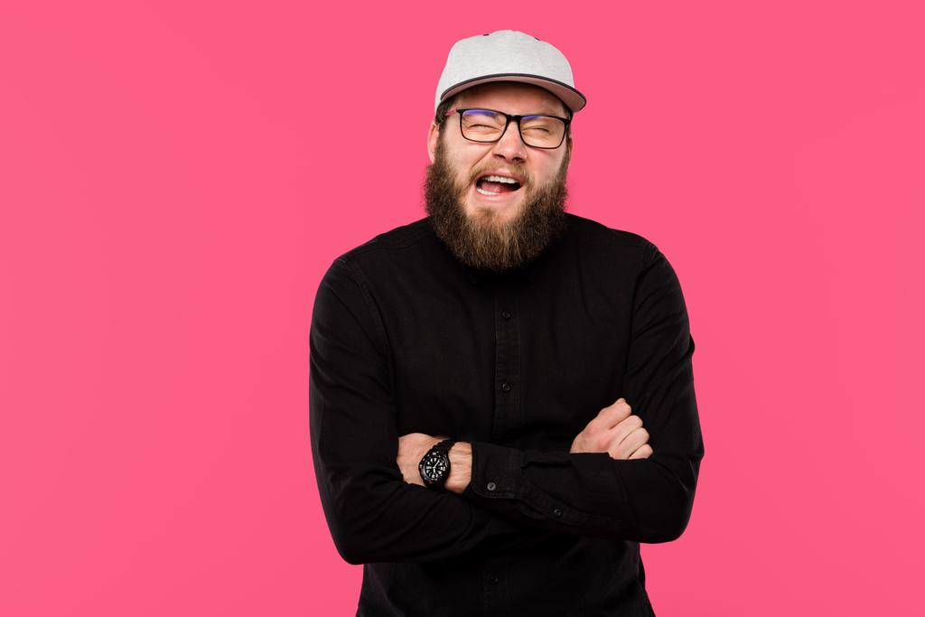 young bearded man with crossed arms doing grimace isolated on pink  - Photo, Image