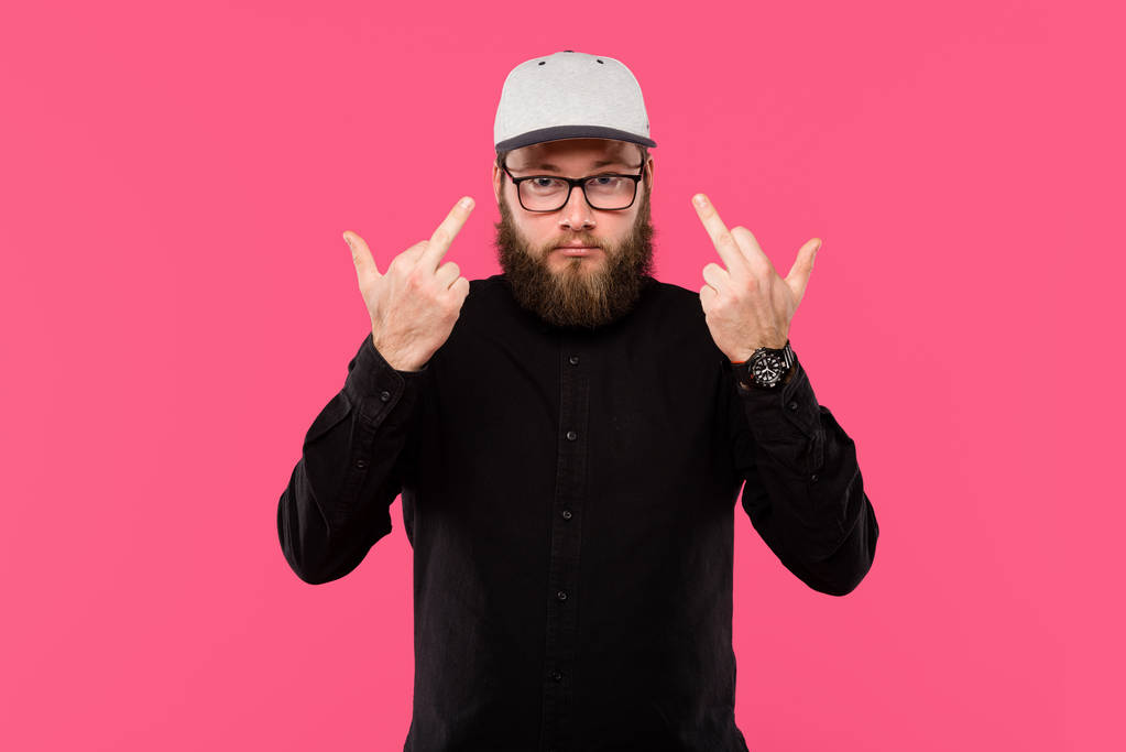 стильный бородатый мужчина в очках, показывающий средний палец, изолированный на розовом
 - Фото, изображение