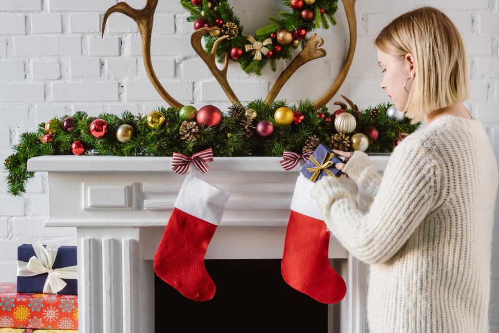 mujer joven poniendo regalo en la media de Navidad en la chimenea
 - Foto, imagen