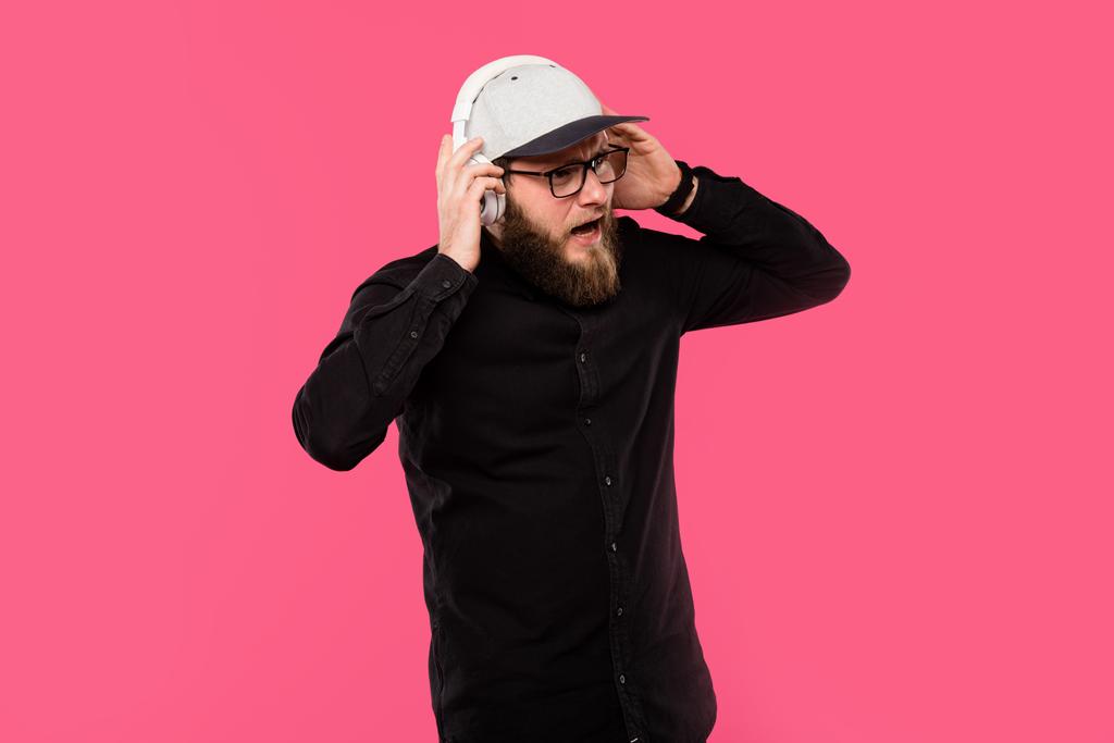απογοητευμένος γενειοφόρος hipster αρσενικών απογειώνεται ακουστικά που απομονώνονται σε ροζ - Φωτογραφία, εικόνα