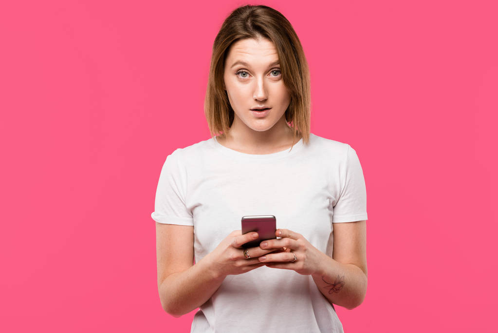 jonge vrouw met smartphone kijken camera geïsoleerd op roze - Foto, afbeelding
