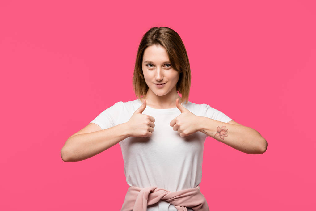 smiling tattooed girl showing thumbs up gesture isolated on pink - Photo, Image