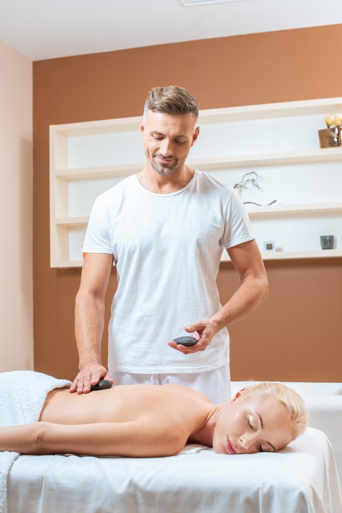 Yakışıklı terapist spa salonda taş masaj yapıyor  - Fotoğraf, Görsel