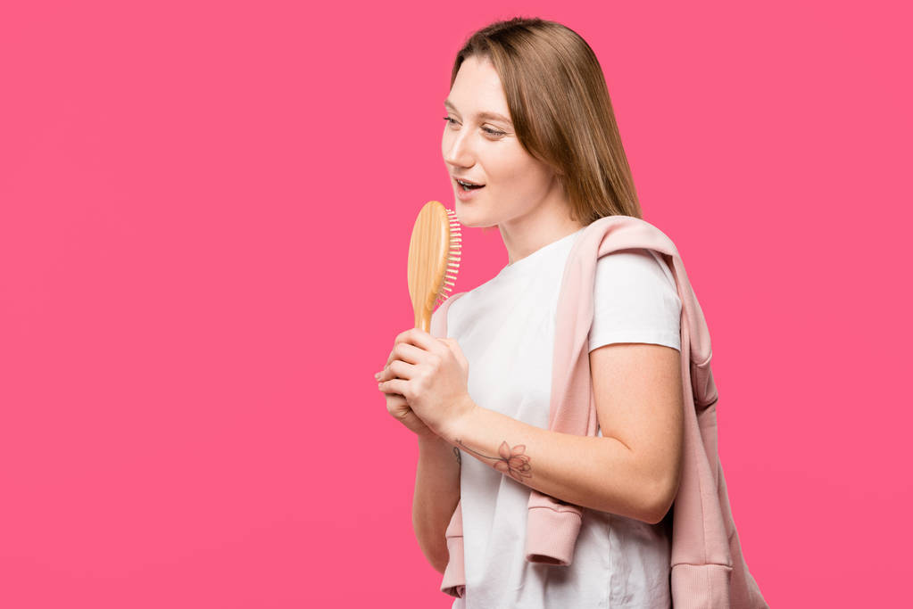 όμορφη νεαρή γυναίκα εκμετάλλευση βούρτσα και ένα τραγούδι που απομονώνονται σε ροζ  - Φωτογραφία, εικόνα