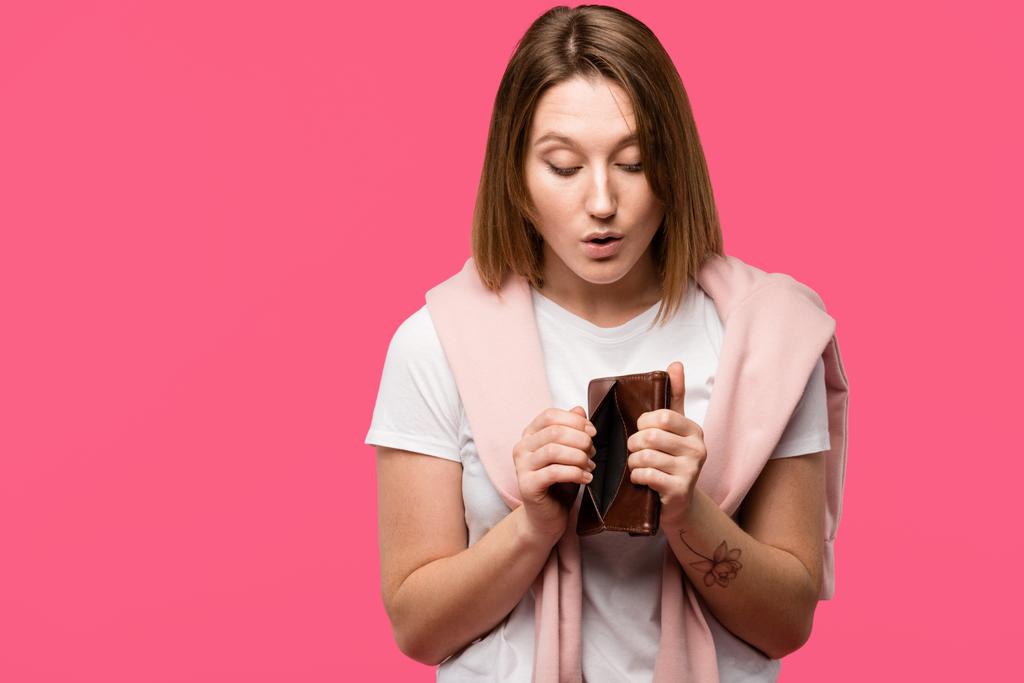 шокована молода жінка, дивлячись на порожній гаманець ізольовано на рожевому
 - Фото, зображення