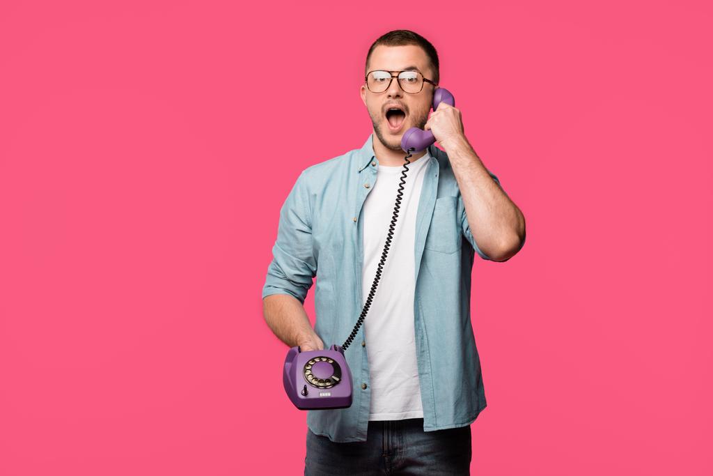 Šokovaný muž v brýlích mluví vintage telefonicky a při pohledu na fotoaparát izolované na růžové - Fotografie, Obrázek