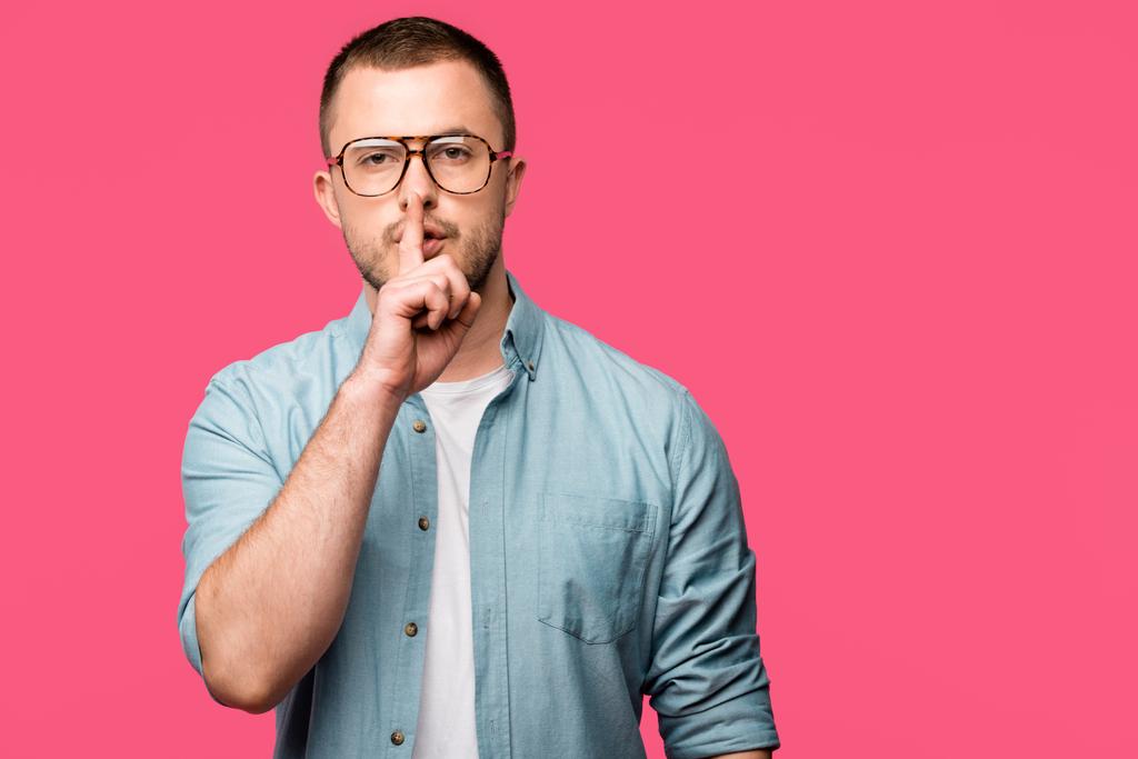 young man gesturing for silence with finger on lips and looking at camera isolated on pink - Photo, Image