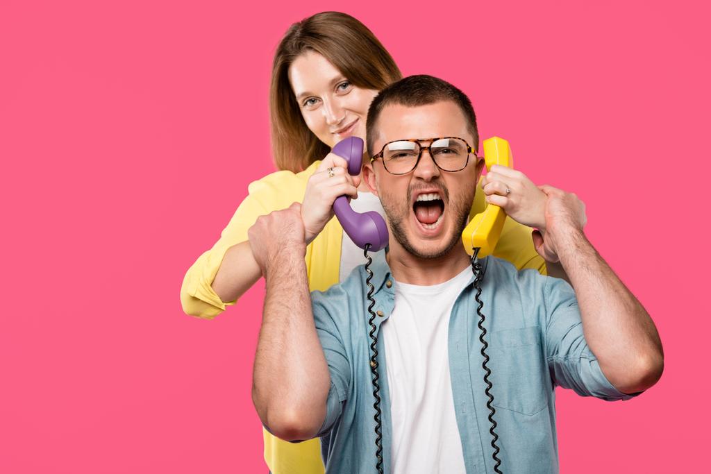 mladá žena držící telefonů a muž v brýlích křik izolované na růžové  - Fotografie, Obrázek